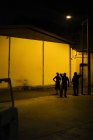 MALAYSIA- April 21, 2016: Distant view of three men standing under lantern on near buildings at night street scene — Stock Photo