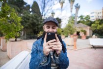 Portrait of man in stylish outfit taking photo with smartphone on background of street. — Stock Photo