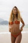 Smiling blonde girl in bikini walking on beach and looking at camera — Stock Photo