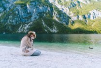 Жінка сидить на березі озера і дивиться на камеру — стокове фото