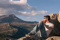 Relaxed young man sunbathing on top of the mountain at sunset — Stock Photo