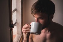 Продуманий молодий чоловік п'є каву і дивиться на вікно — стокове фото
