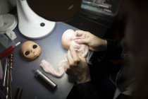 Sopra la spalla vista delle mani dell'artista applicare i capelli sulla testa della bambola a tavola — Foto stock