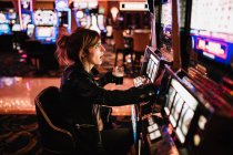Seitenansicht einer Frau, die im Casino sitzt und Spielautomaten spielt. — Stockfoto