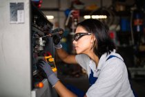 Vue latérale du mécanicien féminin dans googles à l'aide d'un tournevis pour fixer le moteur du compresseur — Photo de stock