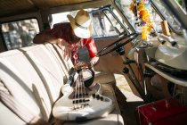 Man in cowboy hat putting electric bass guitar on front seat of retro van — Stock Photo