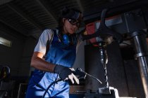 Low angle portrait of female mechanic using air blow gun to clean shavings from column type drill — Stock Photo