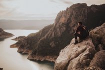 Молодой путешественник любуется диллическим пейзажем сидя на скале — стоковое фото