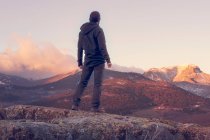Uomo in cima alla montagna in piedi sulla roccia a guardare una bella alba nella soleggiata montagna innevata — Foto stock