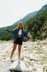 Chica rubia posando sobre piedras de la orilla del río - foto de stock