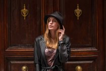Молодая девушка в шляпе смотрит в сторону, позируя перед украшенными дверями — стоковое фото