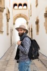 Бородатий чоловік з позує з рюкзаком і дивиться через плече на камеру на вулиці . — стокове фото