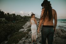 Женщина смотрит через плечо на мужчину, стоящего спиной к каменистой тропической береговой линии — стоковое фото