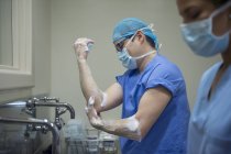 Vista lateral de los médicos en uniforme lavándose las manos antes de la operación - foto de stock
