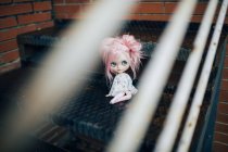 Vue à travers les mains courantes à poupée aux cheveux roses assis sur les escaliers — Photo de stock