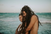 Seitenansicht eines Paares mit Dreadlocks, das sich an der Meeresküste umarmt — Stockfoto