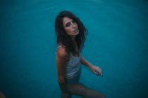 Porträt einer brünetten Frau, die in transparentem blauen Wasser im Pool steht — Stockfoto
