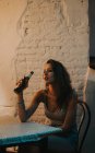 Seitenansicht eines brünetten Mädchens, das am Cafétisch sitzt und Bier trinkt — Stockfoto