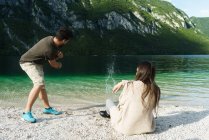 Pareja lanzando piedras al lago de montaña - foto de stock