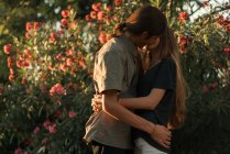 Vista lateral de abrazar a la pareja besándose sobre plantas en flor en el telón de fondo - foto de stock