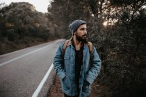Man with backpack walking on country road and looking aside — Stock Photo