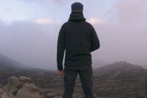 Visão traseira do homem com chapéu nas montanhas no dia nublado — Fotografia de Stock