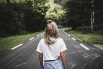 Visão traseira da mulher andando na estrada na floresta — Fotografia de Stock