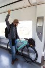 Bearded man with backpack holding bike in train wagon — Stock Photo