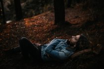 Vista lateral de una persona acostada en el suelo en los bosques de otoño . - foto de stock