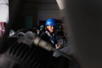Female mechanic wearing hardhat operating hoist at workshop — Stock Photo