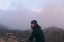 Uomo con cappello in montagna una giornata fredda e nuvolosa — Foto stock