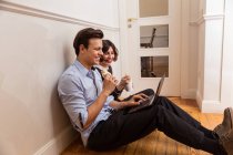 Seitenansicht junger fröhlicher Freunde in Freizeitkleidung, die mit Laptop auf dem Boden sitzen, während sie Wok essen — Stockfoto