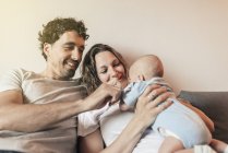 Happy couple with newborn baby on coach at home — Stock Photo