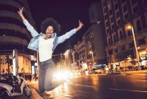 Beautiful young black woman jumping in city street at night — Stock Photo