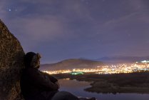 Людина на вершині гори і насолоджуватися видом на нічне небо і міські вогні — стокове фото