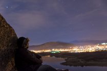 Uomo sulla cima di una montagna e godendo di vista sul cielo notturno e le luci della città — Foto stock