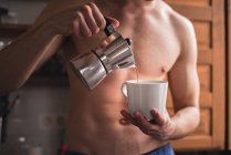 Mittelteil des hemdslosen Mannes gießt Kaffee in weißen Becher. — Stockfoto