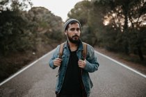Man with backpack standing on road and looking aside — Stock Photo