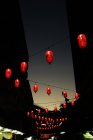Low angle view of red Chinese lanterns hanging on ropes between buildings in dawn. — Stock Photo