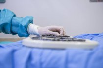 Обрезанное изображение руки хирурга, берущего медицинское оборудование с подноса на столе — стоковое фото