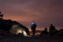 Hombre en la cima de una montaña y disfrutando de la vista del cielo nocturno y las luces de la ciudad - foto de stock