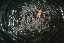 Draufsicht einer jungen Frau im orangefarbenen Bikini, die im Sonnenlicht im Wasser schwimmt — Stockfoto