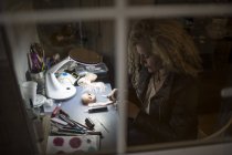 Vista através da janela de bonecas mulher crafting à mesa — Fotografia de Stock