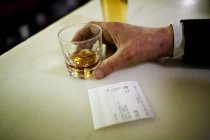 Ernte männliche Hand hält Glas mit alkoholischen Getränken auf Theke mit Schein in der Nähe liegend. — Stockfoto