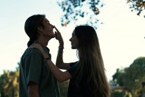 Vue latérale de la jeune fille brune touchant les copains nez avec le doigt au parc — Photo de stock
