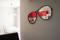 Espelho em forma de óculos de sol pendurado na parede e refletindo inetrior da cozinha — Fotografia de Stock
