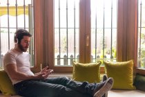 Giovane uomo che ascolta musica con tablet rilassato a casa con la finestra illuminata dalla calda luce del sole — Foto stock