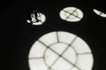 Vista de ángulo alto de una pareja anónima cogida de la mano y caminando en el pasillo con puntos de luz de círculo y sombras de ventanas . - foto de stock
