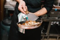 Mid section view of cook holding pan with ingredients and spatula at restaurant kitchen — Stock Photo