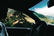 Side view of unrecognizable person driving car along mountain landscape. — Stock Photo